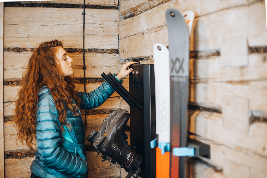 customer in cabin rental turning on ski boot dryer after storing her skis on cliq ski storage wall clip